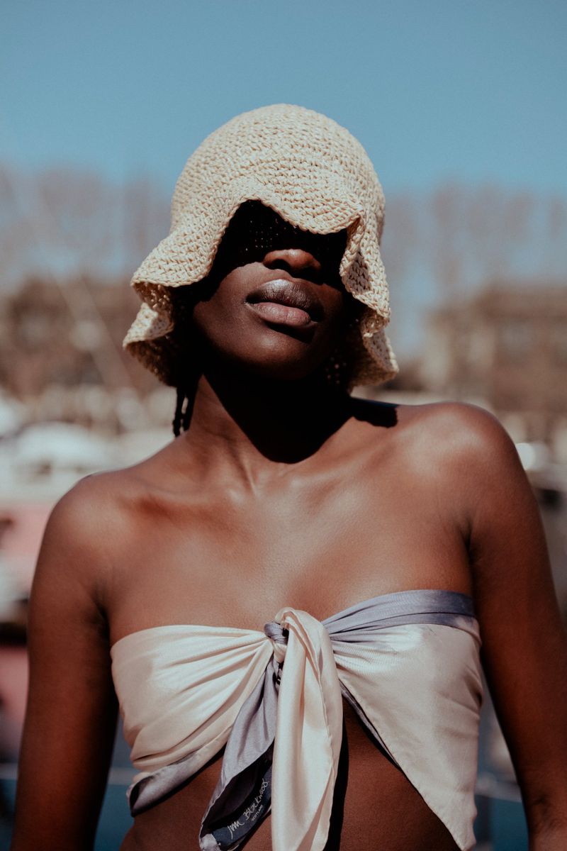 Close-up shot of an African-American woman in a scarf top and a sunhat casting shadows on her face outdoors on a bright day.