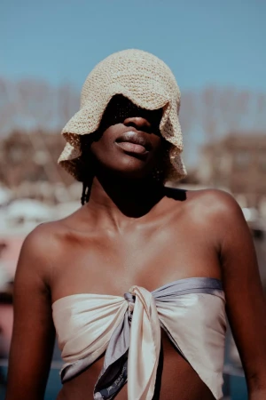 Close-up shot of an African-American woman in a scarf top and a sunhat casting shadows on her face outdoors on a bright day.