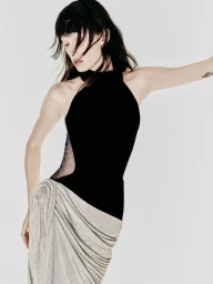 Model wearing a black sleeveless halter top and draped silver textured skirt with a hip rosette against a white background.