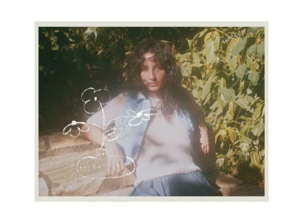 Woman in a denim vest seated outdoors amidst foliage with a white line-drawn flower illustration overlaid in the foreground.