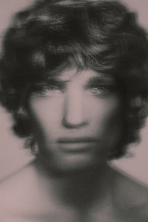 Soft-focus close-up portrait of a young man with dark wavy hair looking directly forward against a muted backdrop.