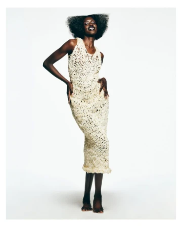 Black woman with a sculptural afro wearing an off-white textured crochet midi dress against a white seamless background.