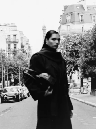 Model Selina Pillay in a black coat holding a handbag on a Paris street with the Eiffel Tower in the background.