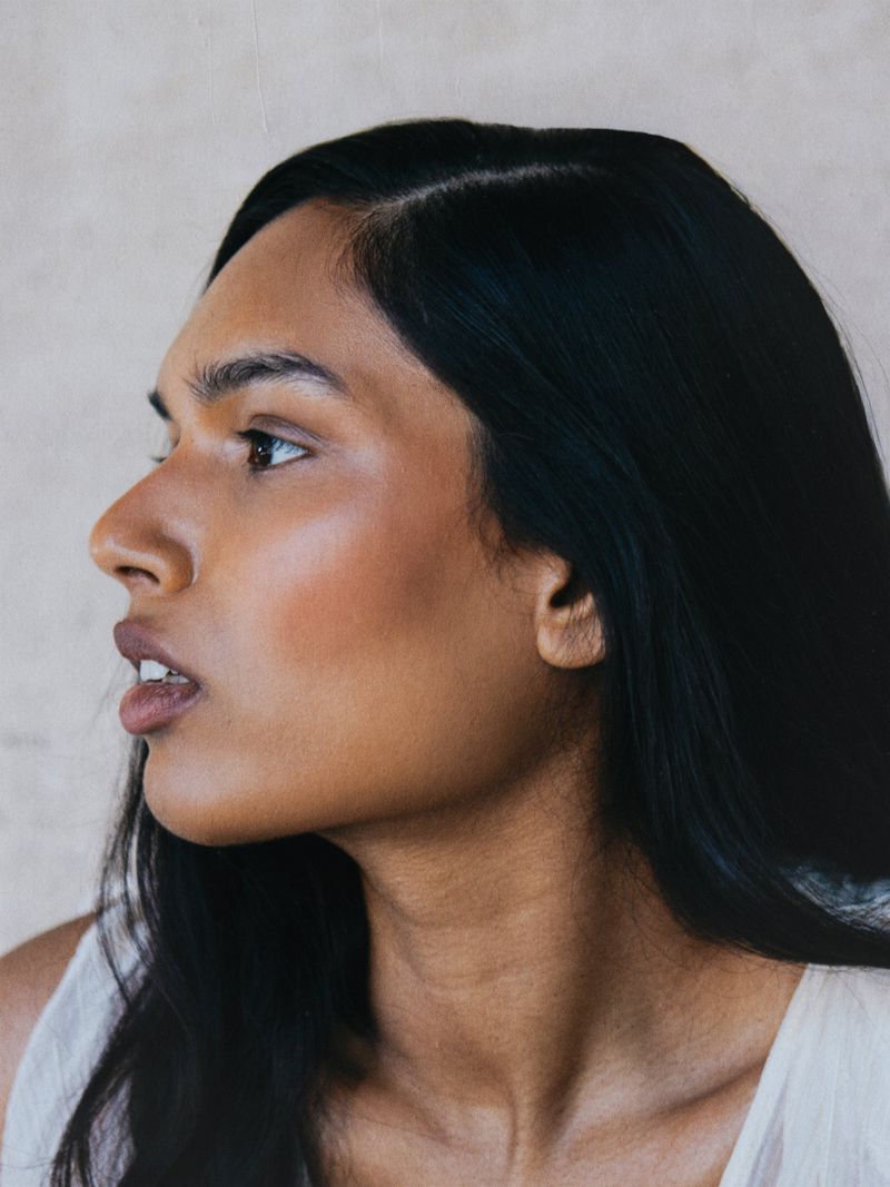 Side profile beauty portrait of model Selina Pillay with long dark hair looking left against a neutral backdrop.