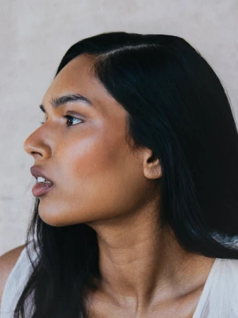 Side profile beauty portrait of model Selina Pillay with long dark hair looking left against a neutral backdrop.