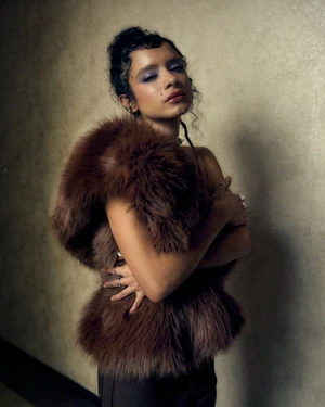 Portrait of a woman wearing a voluminous brown fur stole with crossed arms against a textured backdrop for Acero Magazine.