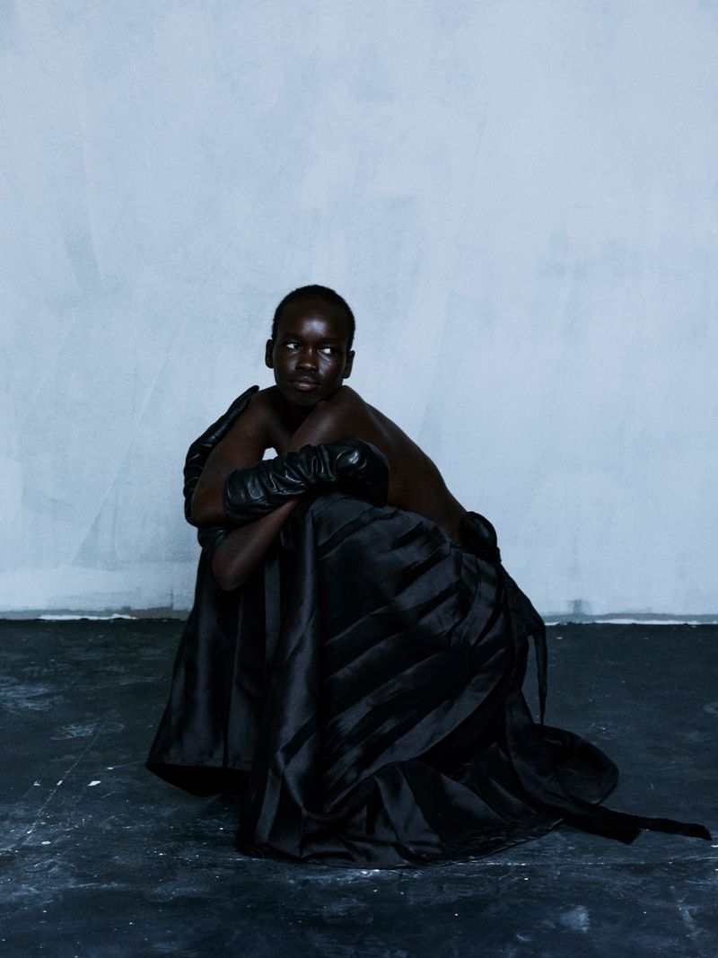 Model Akuel Malong seated in a voluminous black gown and leather gloves against a cool textured wall