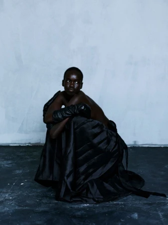 Model Akuel Malong seated in a voluminous black gown and leather gloves against a cool textured wall