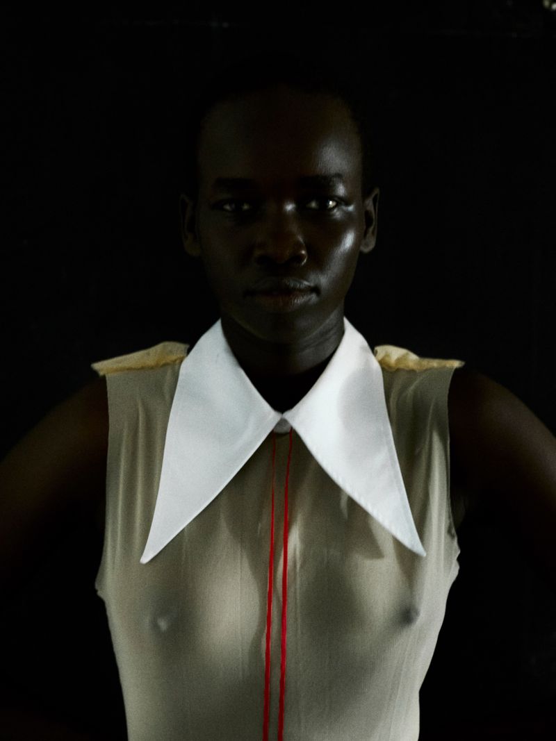 Model Akuel Malong wearing a sleeveless beige top with an exaggerated white pointed collar against a black background.