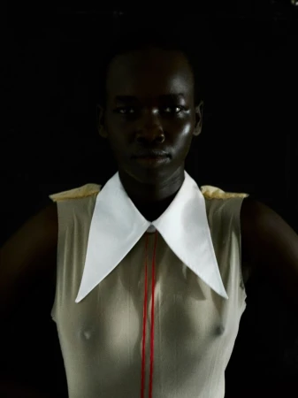 Model Akuel Malong wearing a sleeveless beige top with an exaggerated white pointed collar against a black background.