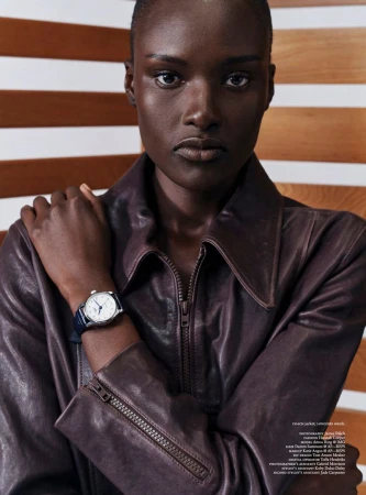 Model Amou Ring posing in a dark brown leather jacket and wristwatch against a background of horizontal wooden slats.