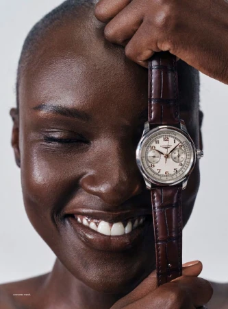 Close-up portrait of model Amou Ring smiling with closed eyes while holding a brown leather strap wristwatch in front of her face.