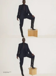 Model Amou Ring posing in a dark tailored suit and high knee boots with one foot on a wooden block against a white studio background.