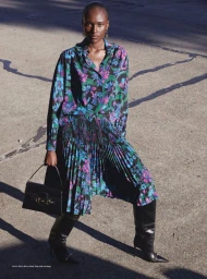 Model Amou Ring posing outdoors in a floral print shirt, pleated skirt, black knee-high stiletto boots, holding a black handbag.