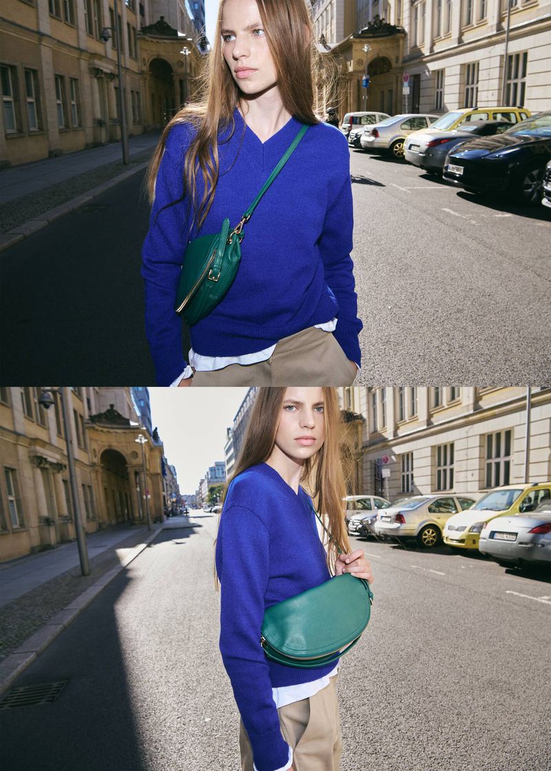 Model Valerie Margareta wearing a royal blue v-neck sweater and green crossbody bag on a sunny city street for Mango.