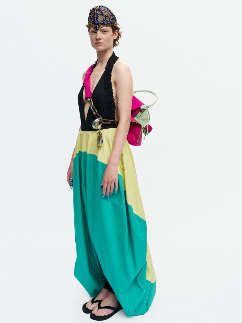 Model Bella Berghoef in a green and yellow colorblock skirt, black halter top, and pink backpack against a white backdrop.