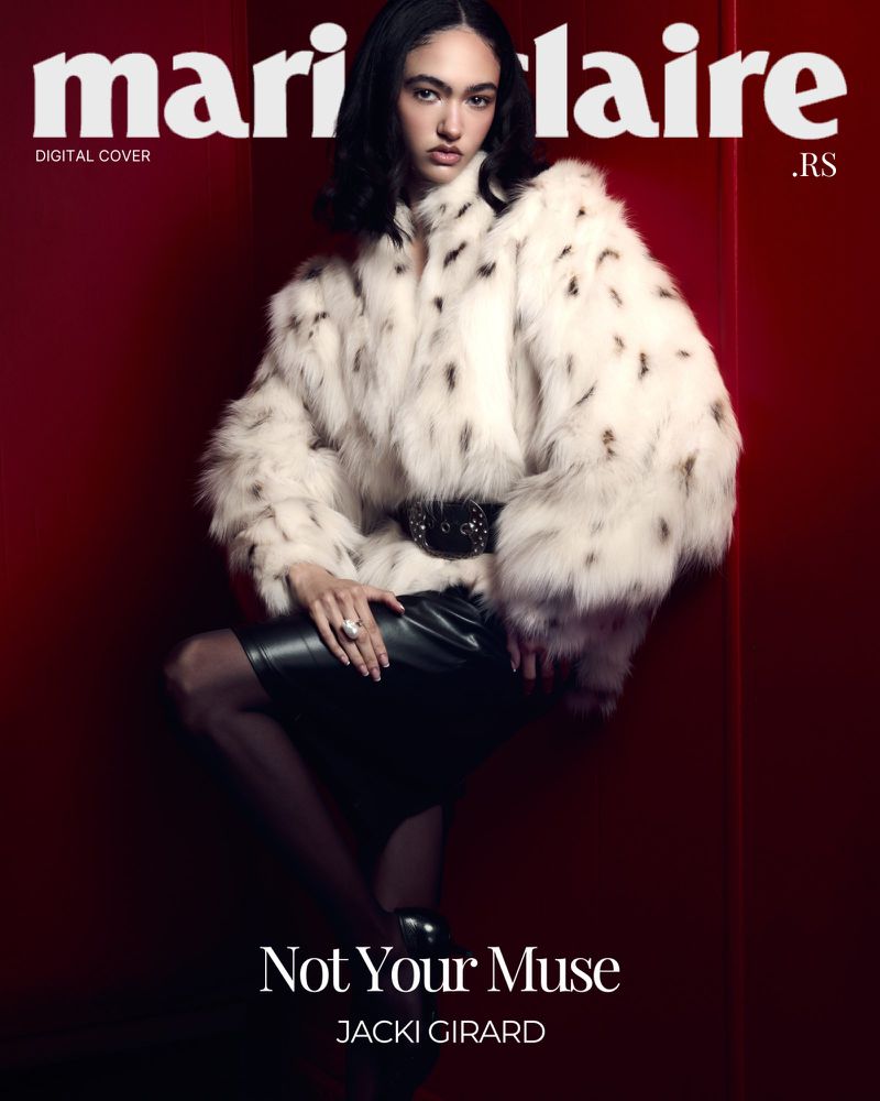 Model Jacki Girard wearing a voluminous white spotted fur coat with a wide black belt against a deep red studio backdrop.