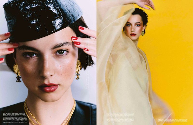Editorial fashion close-up of a female model with red lipstick, wearing a black hat and jewelry, and a woman in yellow sheer clothing.