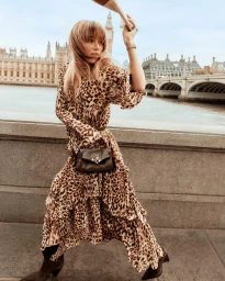 Woman in a flowing leopard-print maxi dress and ankle boots walking along a stone embankment with Big Ben in the background.
