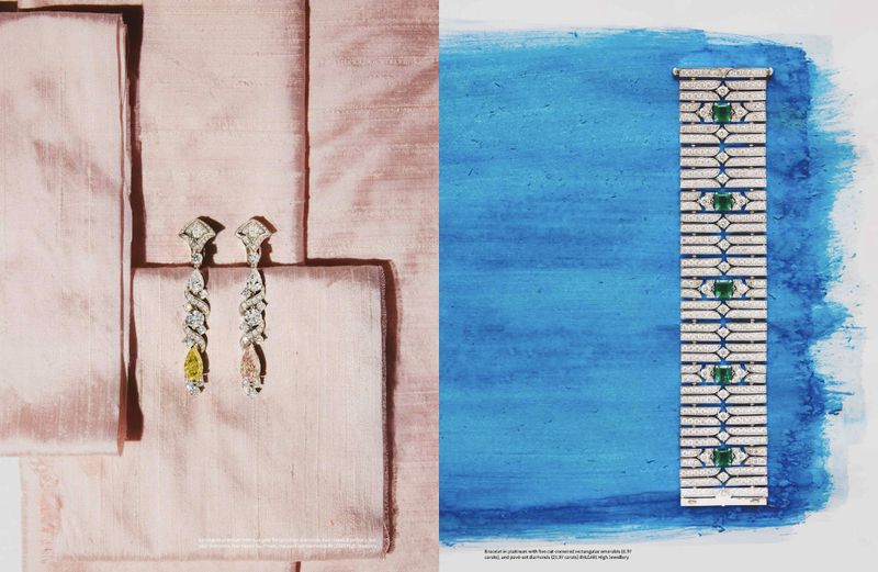High-end jewelry layout: diamond earrings on pink silk, platinum bracelet with emeralds on blue paint background. Studio lighting.