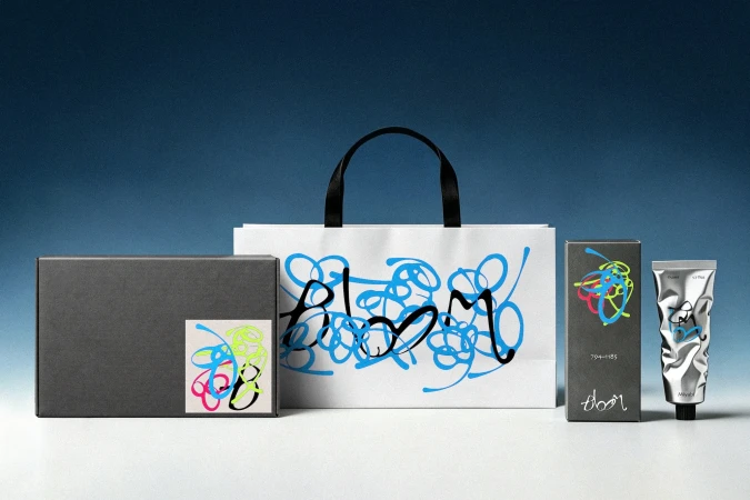 Branded packaging mockup for Bloom featuring a white shopping bag, dark box, carton, and metallic cosmetic tube with blue scribble art.
