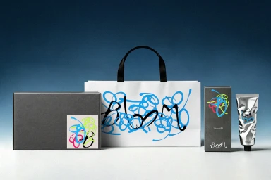 Bloom brand packaging suite including a matte black gift box, branded white paper bag, product carton, and metallic squeeze tube.