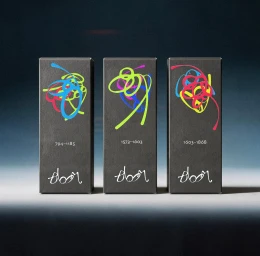 Three matte black packaging boxes with colorful abstract line illustrations and Bloom logos in a row on a studio surface.