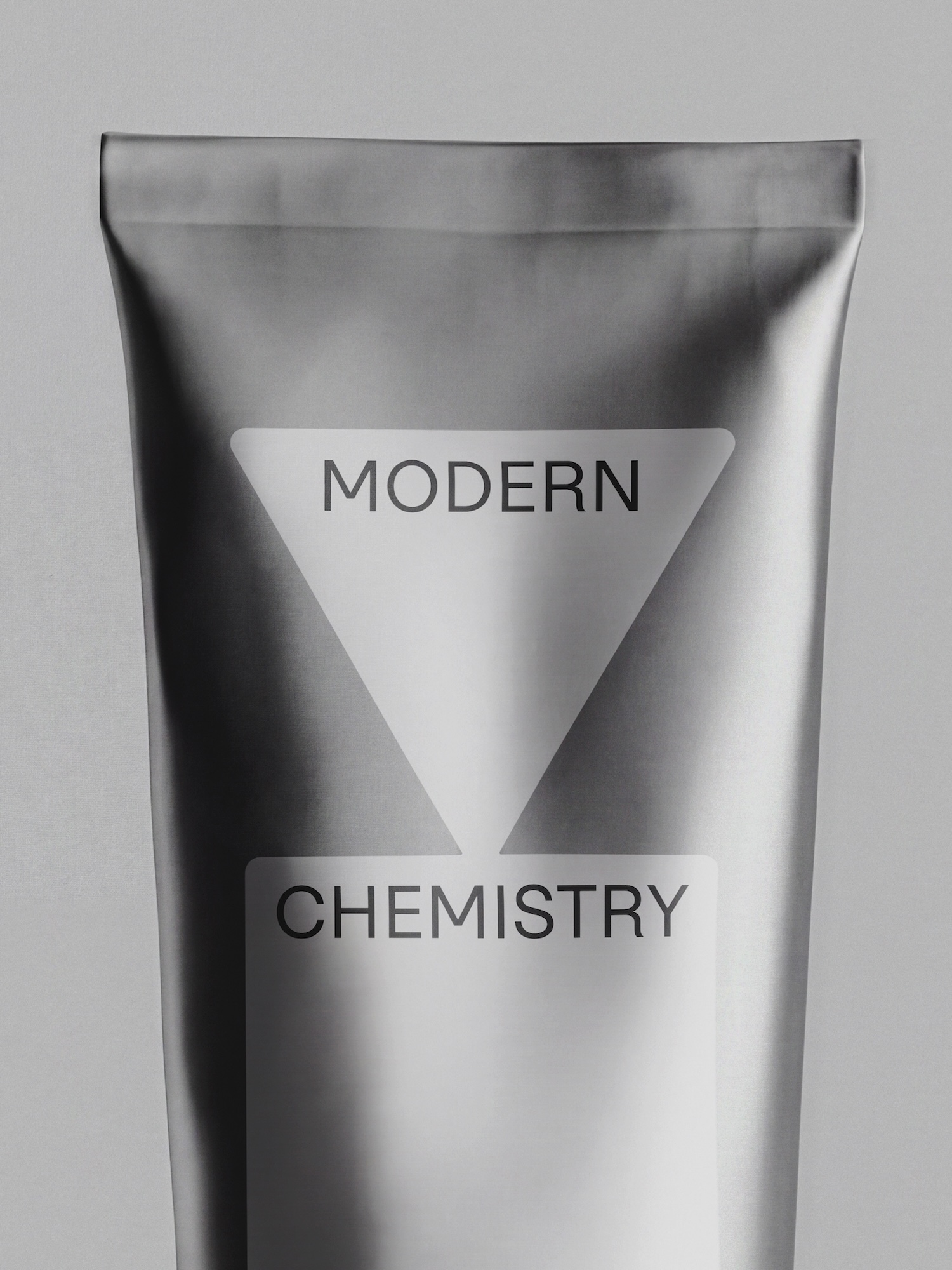 Close-up of a matte metallic grey squeeze tube packaging printed with Modern Chemistry branding against a solid light grey background.