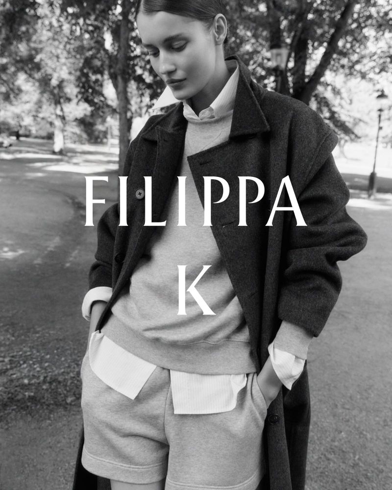 Model wearing a layered collared shirt, crewneck sweater, shorts, and an oversized coat in black and white for Filippa K.