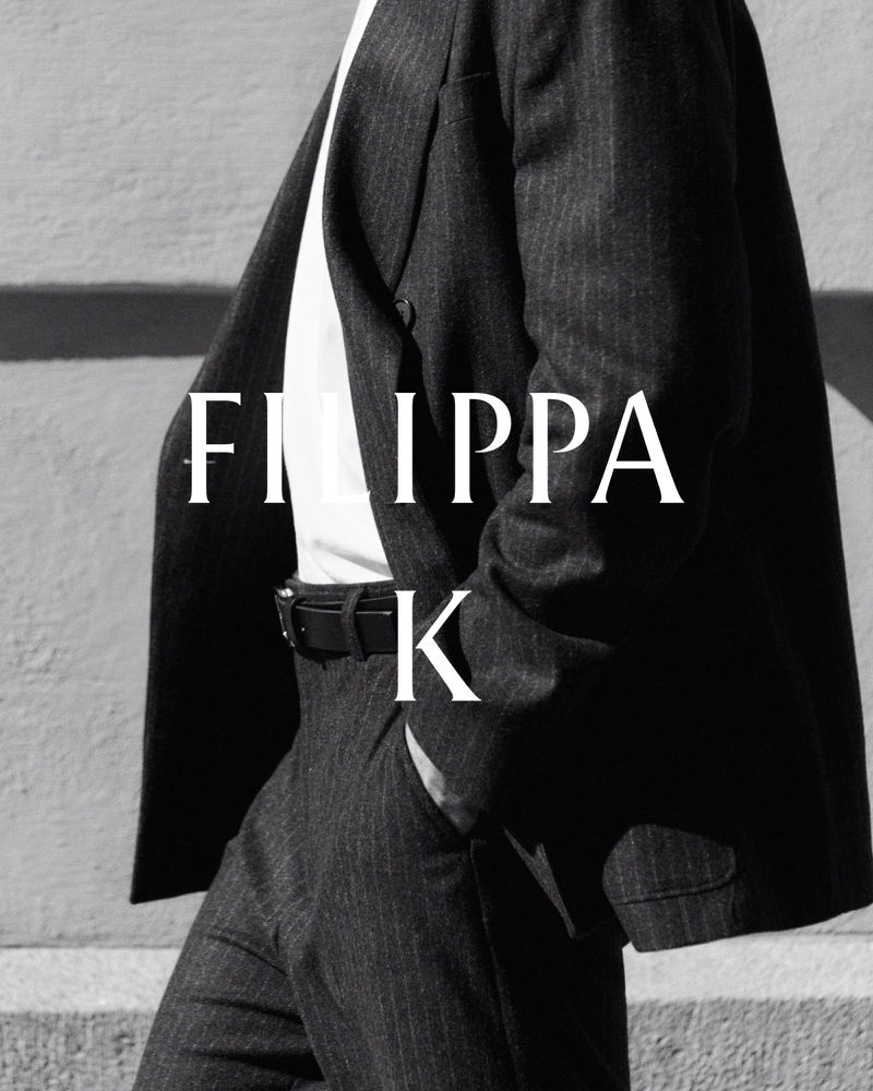 Model wearing a dark pinstripe suit jacket, trousers, white top, and black belt with Filippa K logo overlay.