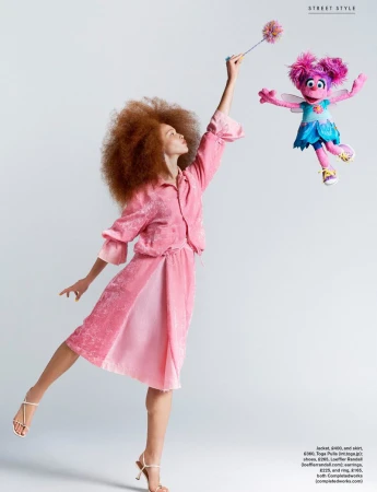 Model Tianna St. Louis wearing a pink dress and holding a wand toward a floating Abby Cadabby puppet against a white background.