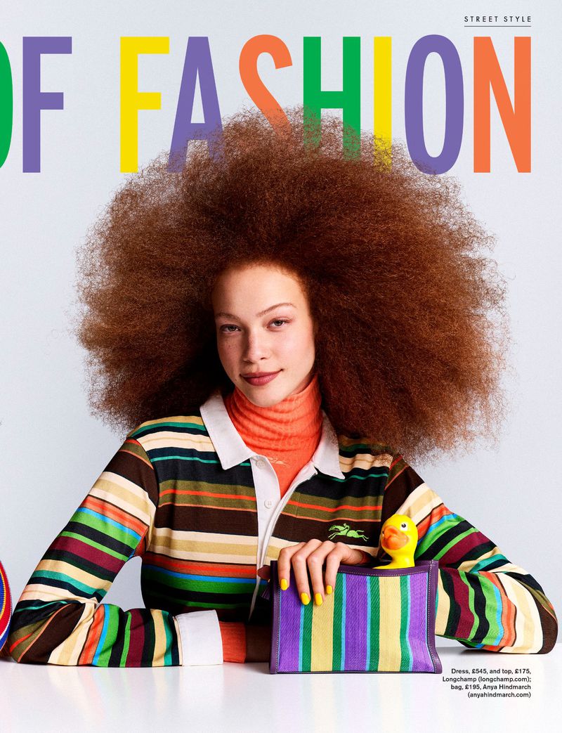 Model Tianna St. Louis with voluminous auburn afro hair posing with a striped clutch bag and yellow rubber duck against a white backdrop.