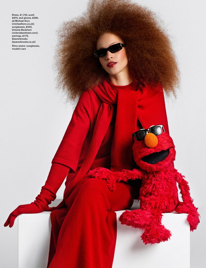 Model Tianna St. Louis in an all-red outfit and sunglasses seated with an Elmo puppet against a white background.