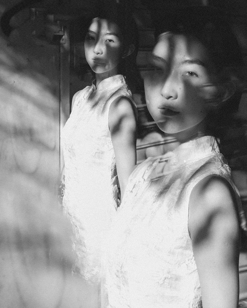 Black and white multiple exposure portrait of an Asian woman in a light textured sleeveless dress with dappled shadows on her face.
