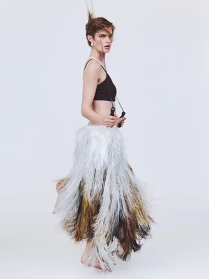 Model posing in a black crop top and a voluminous tiered fringe skirt while holding a jump rope against a white backdrop.