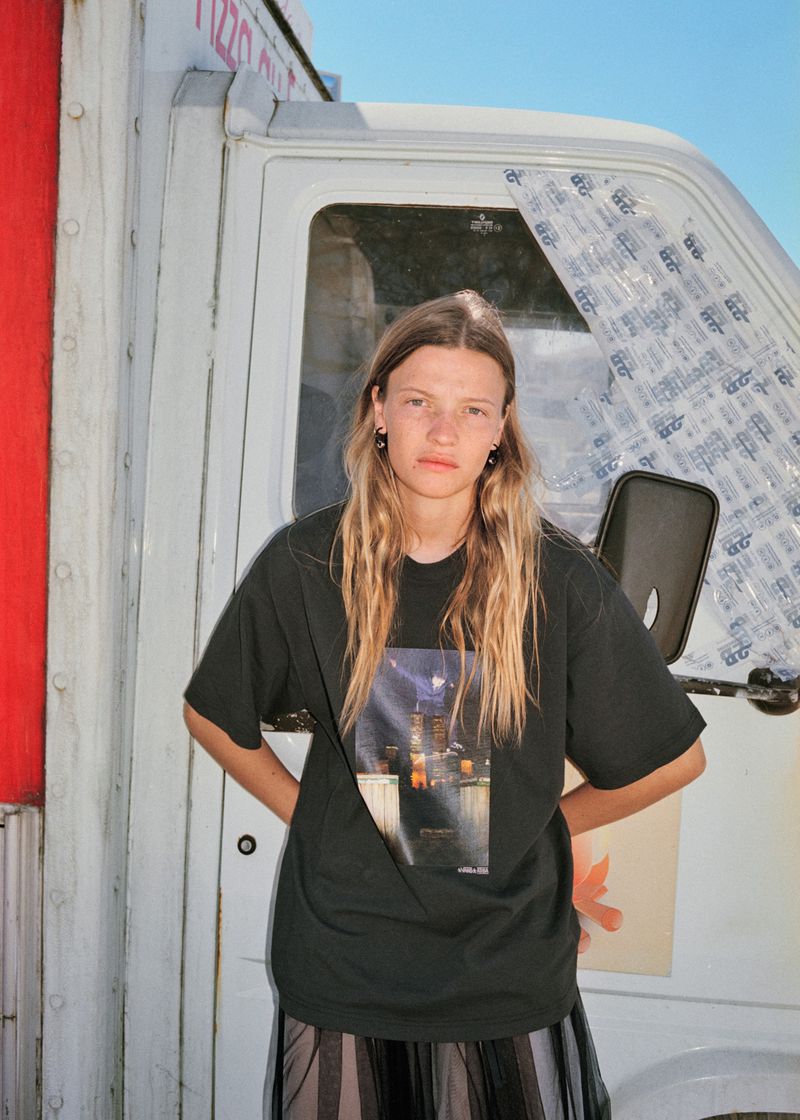 Woman in an oversized black graphic t-shirt posing in front of a white utility truck against a blue sky.