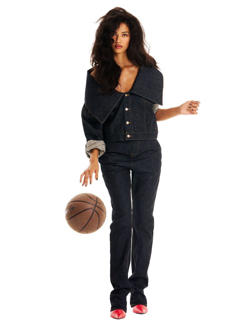 Model Jessie Aina in a dark denim set with an exaggerated folded collar posing with a basketball on a white background.