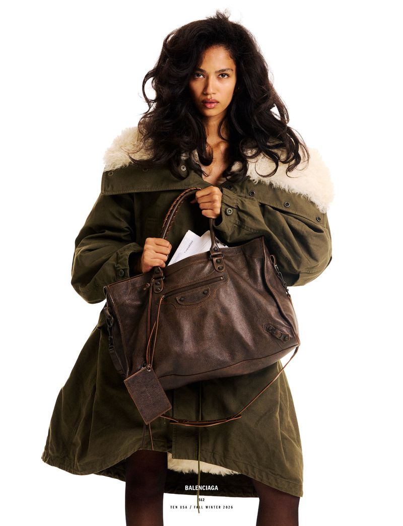 Model Jessie Aina holding a large brown leather Balenciaga bag while wearing an oversized olive parka with a shearling collar.