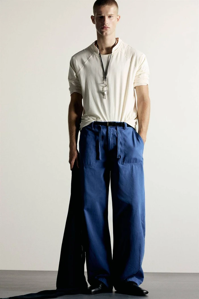 Male model wearing an off-white t-shirt and wide-leg royal blue trousers against a neutral studio background.