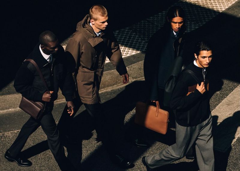 Four male models in tailored coats and designer bags walking across a sunlit street for Louis Vuitton Formal.