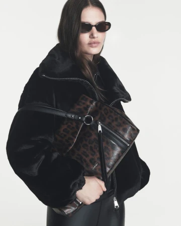 Model Emmi Freeman in black faux-fur jacket and sunglasses holding a leopard print shoulder bag against a white studio background.