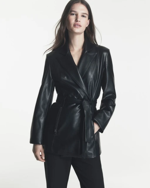 Emmi Freeman posing in a belted black leather jacket and trousers against a white studio background for DKNY.