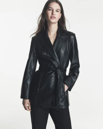 Emmi Freeman posing in a belted black leather jacket and trousers against a white studio background for DKNY.