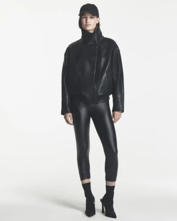 Model wearing a black oversized leather jacket, black leggings, baseball cap, and pointed heels against a white background.