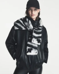Model Emmi Freeman in a black leather jacket, black cap, and black-and-white zebra knit scarf against a white background.