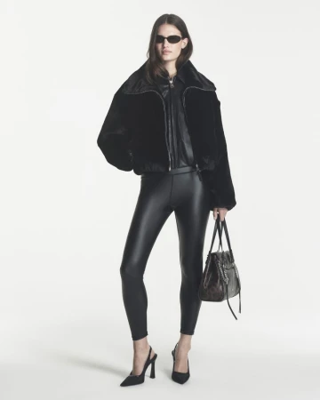 Model wearing a black cropped jacket, black leggings, sunglasses, and slingback heels holding a black tote on a white background.