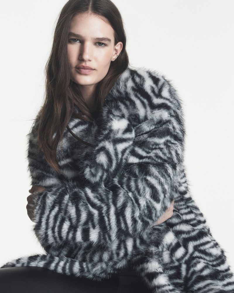 Model Emmi Freeman posing in a black and white animal print faux fur coat against a plain white studio background.
