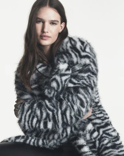 Model Emmi Freeman posing in a black and white animal print faux fur coat against a plain white studio background.