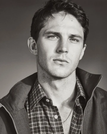 Monochrome portrait of model Tommy Hackett wearing a plaid shirt and open jacket against a neutral studio backdrop.