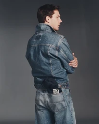Model Tommy Hackett seen from behind wearing a blue denim jacket and matching jeans against a grey studio backdrop.